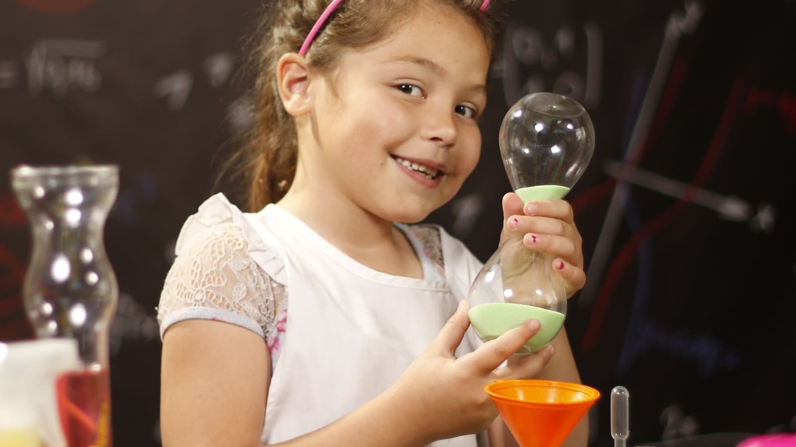 A child smiling while holding glassware at a science experiment table